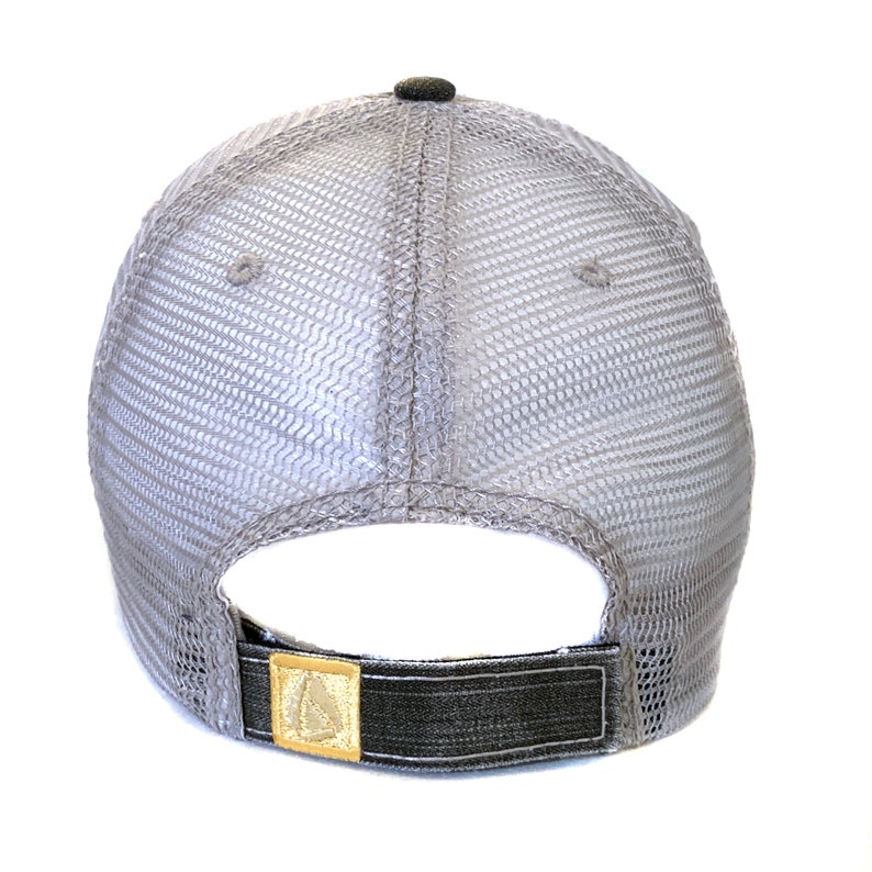 May include: A gray trucker hat with a mesh back and a dark gray brim. The hat features a small, dark gray button on top and a gold-colored patch on the adjustable strap.