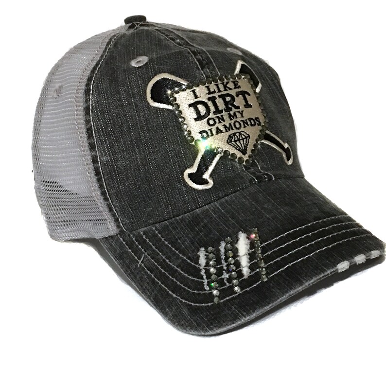 May include: A black and gray distressed baseball cap with a mesh back. The cap has a silver and black patch with rhinestones that says "I Like Dirt On My Diamonds" with a baseball bat and crossed bones.