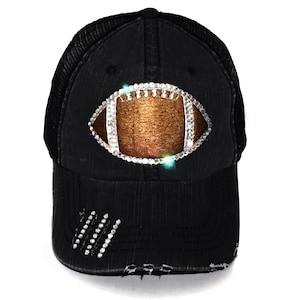 May include: Black distressed trucker hat with a rhinestone football design. The football is outlined in rhinestones and has a brown leather texture.
