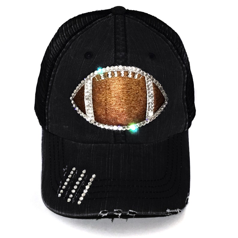 May include: Black distressed trucker hat with a rhinestone football design. The football is outlined in rhinestones and has a brown leather texture.