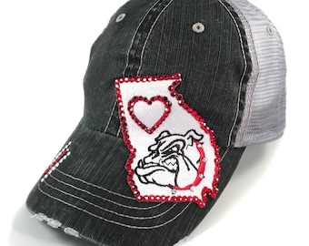 May include: Black and gray distressed denim trucker hat with a red and white embroidered patch of the state of Georgia with a red heart and a bulldog. The hat has a mesh back.