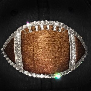 May include: A black baseball cap with a brown leather football design outlined with clear rhinestones.