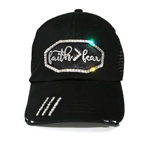 Puede incluir: Gorra de camionero negra con un aspecto desgastado. La gorra tiene un dise&ntilde;o de diamantes de imitaci&oacute;n plateados que dice "faith>fear".
