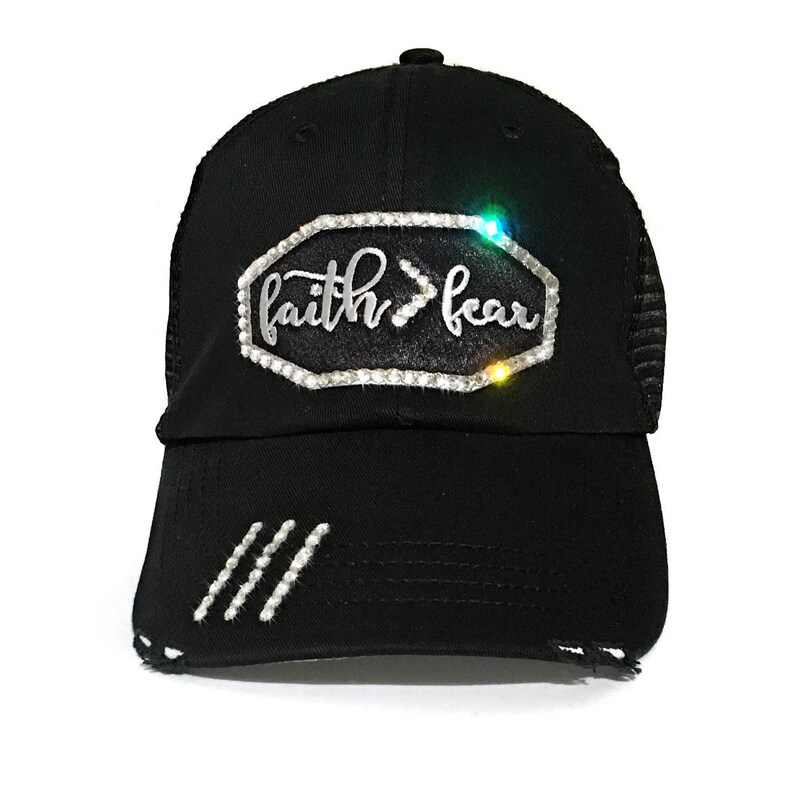 Puede incluir: Gorra de camionero negra con un aspecto desgastado. La gorra tiene un dise&ntilde;o de diamantes de imitaci&oacute;n plateados que dice "faith>fear".