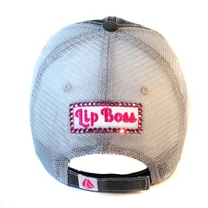 May include: Gray and black mesh baseball cap with a pink and white embroidered patch that says "Lip Boss" with rhinestones.