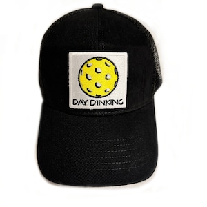 Puede incluir: Gorra de camionero negra con un parche amarillo y blanco que dice "Day Dink'n" y una imagen de dibujos animados de una pelota de pickleball amarilla.