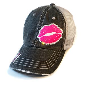 May include: A black and gray trucker hat with a pink rhinestone lips design.
