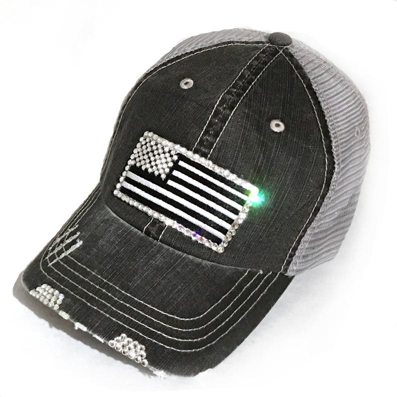 May include: A black and gray distressed baseball cap with a mesh back. The cap features a rhinestone American flag design.