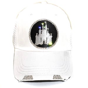 Puede incluir: Gorra de b&eacute;isbol blanca con un parche negro y blanco de un castillo incrustado con diamantes de imitaci&oacute;n.