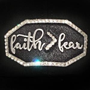 Puede incluir: Gorra de b&eacute;isbol negra con un parche bordado blanco que dice "faith>fear" rodeado de diamantes de imitaci&oacute;n.