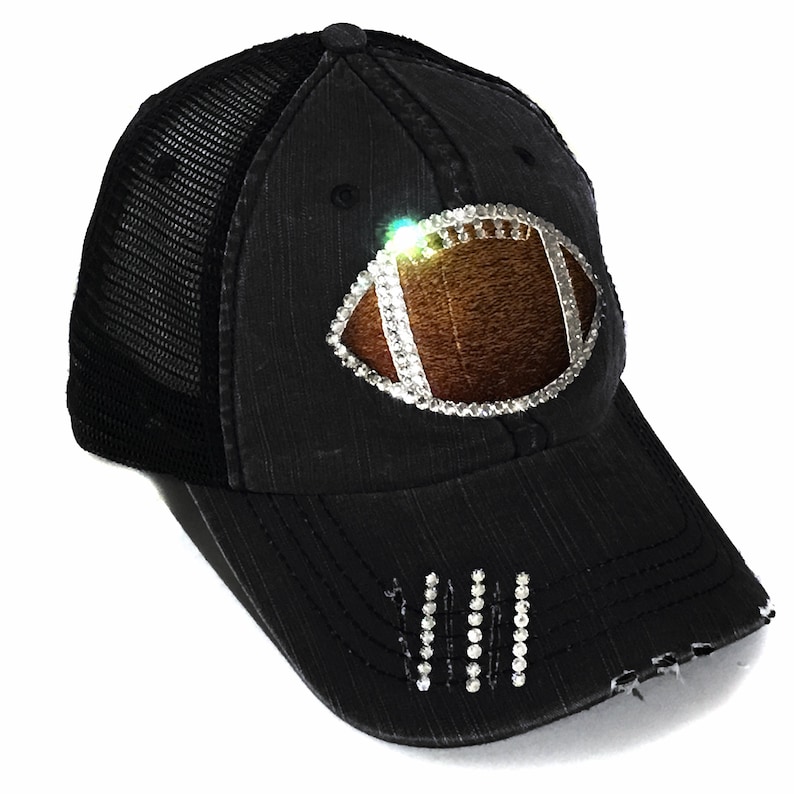 May include: Black trucker hat with a distressed look. The hat has a mesh back and a rhinestone football design on the front.