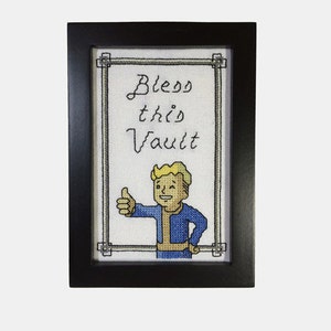 May include: A framed cross-stitch design featuring a cartoon character giving a thumbs up with the text "Bless this Vault".