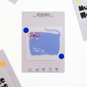 Könnte beinhalten: Eine hellgraue Karte zeigt eine blaue Katze mit roter Brille und dem Text "Just a cool cat." Weitere Karten mit Text und farbigen runden Aufklebern sind im Bild zu sehen.