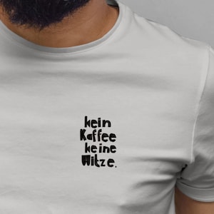 Puede incluir: Una camiseta gris claro con el texto alemán "kein Kaffee keine Witze" impreso en negro. La camiseta es de cuello redondo y tiene mangas cortas.