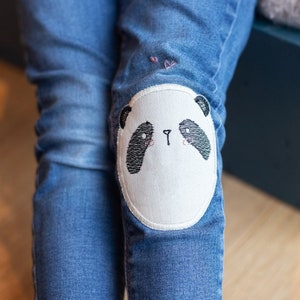 Pode incluir: Jeans azul denim com um remendo de panda branco no joelho.