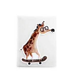Op de afbeelding: Een bruine en beige giraffe met een blauwe hoed en bril rijdt op een zwart skateboard. De giraffe kijkt naar rechts.