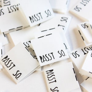 May include: A pile of white fabric labels with black text that reads "PASST SO." The labels are folded and stacked on top of each other.