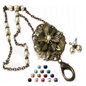 Puede incluir: Un collar de tono dorado con un gran colgante de flor y una cadena con perlas blancas. El collar tiene un cierre de langosta y viene con una variedad de colores de perlas para elegir.