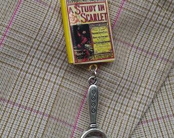 May include: A yellow book charm with the title "A Study in Scarlet" and a magnifying glass charm. The book charm is a miniature version of a classic novel.