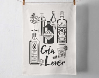 May include: A white kitchen towel featuring a black graphic print of various gin bottles, a cocktail shaker, and two glasses filled with ice and lime wedges. The text Gin Lover is printed in a script font alongside a small illustration of juniper berries.