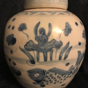 Könnte beinhalten: Eine weiße Keramikvase mit einem blauen und weißen Blumendesign und einem Fisch. Die Vase hat einen Deckel.