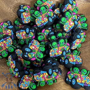 May include: A pile of colorful, psychedelic alien-themed charms. Each charm features two green aliens riding in a van with a peace sign and flowers. The charms are made of silicone and are perfect for adding a touch of whimsy to your jewelry or crafts.