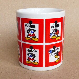 May include: White ceramic mug with a red and white design featuring multiple images of Mickey Mouse in different poses. The mug has a red border around each image.