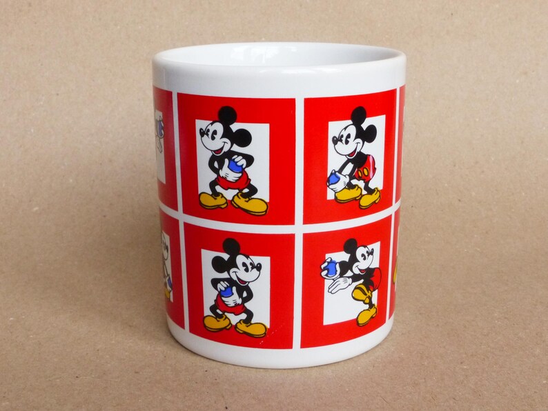May include: White ceramic mug with a red and white design featuring multiple images of Mickey Mouse in different poses. The mug has a red border around each image.