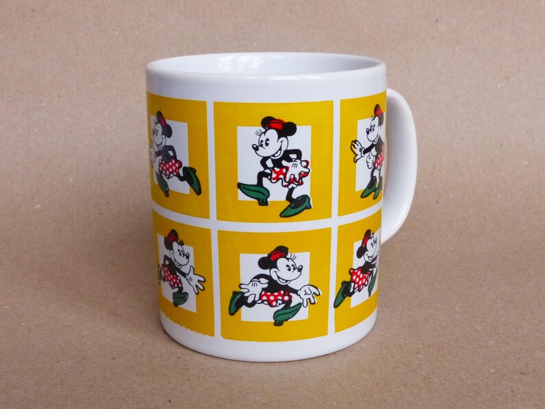 May include: White ceramic mug with a yellow background and multiple images of Minnie Mouse in different poses. Each image is framed in a yellow square.
