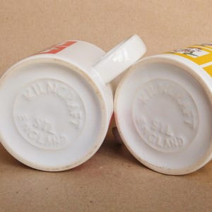 May include: Two white ceramic mugs with a yellow and red design. The bottom of each mug reads "Wilnecraft England".