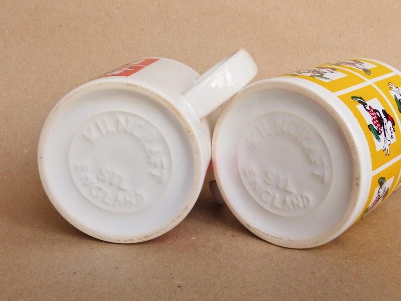 May include: Two white ceramic mugs with a yellow and red design. The bottom of each mug reads "Wilnecraft England".