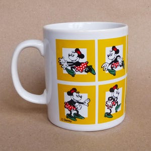 May include: White ceramic mug with a yellow background and a repeating image of Minnie Mouse in a red and white polka dot dress. The mug has a black handle and the text "&copy; Disney" at the bottom.