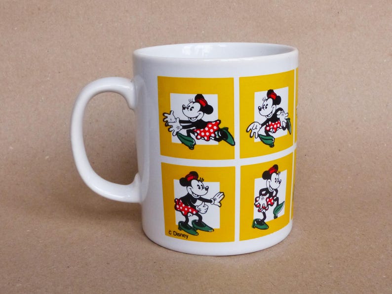 May include: White ceramic mug with a yellow background and a repeating image of Minnie Mouse in a red and white polka dot dress. The mug has a black handle and the text "&copy; Disney" at the bottom.
