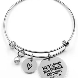 May include: Silver bangle bracelet with three charms: a small pearl, a heart charm, and a round charm with the inscription "She is clothed with strength and dignity Prov 31:25".