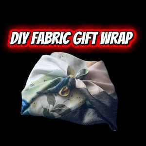 May include: A fabric gift wrap tied in a knot, featuring a floral pattern with shades of white, green, and blue. The text "DIY FABRIC GIFT WRAP" is displayed in red and white. The background is black.