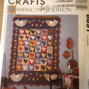 May include: A quilt pattern featuring a patchwork of hearts in red, yellow, blue, and pink. The quilt is framed with a scalloped edge and features a pair of birds on each side. The pattern is titled "American Tradition" and is from McCall's Crafts.