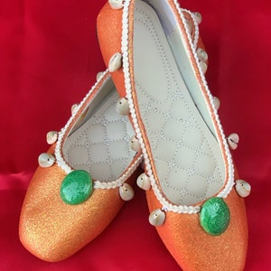 May include: A pair of orange glitter flats with white trim and seashell accents. Each shoe has a green circle embellishment.