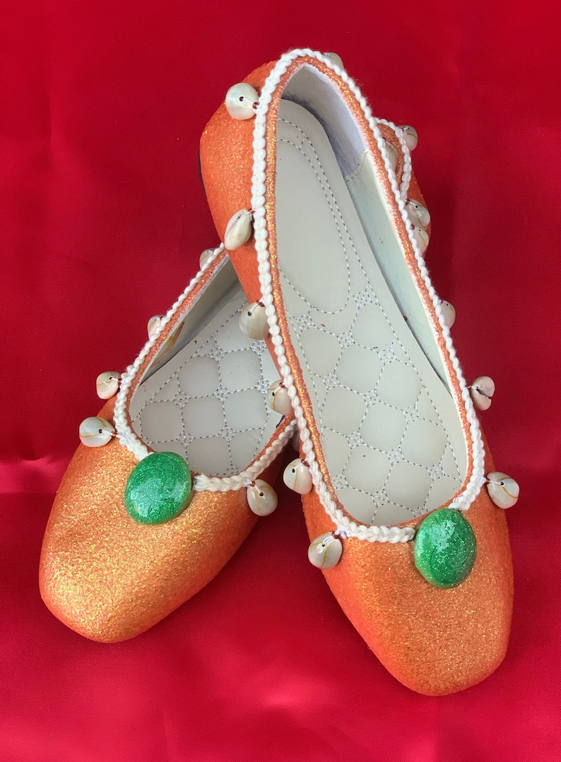 May include: A pair of orange glitter flats with white trim and seashell accents. Each shoe has a green circle embellishment.