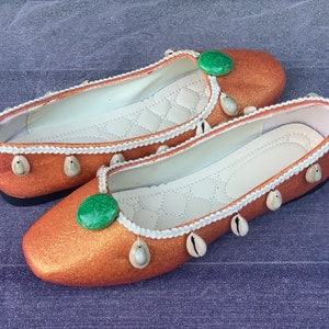May include: A pair of orange glitter ballet flats with white trim and shell accents. Each shoe has a green stone embellishment.
