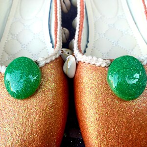 May include: A pair of gold glitter ballet flats with green shell embellishments and white trim.