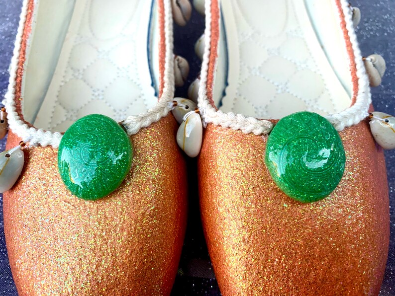 May include: A pair of gold glitter ballet flats with green shell embellishments and white trim.