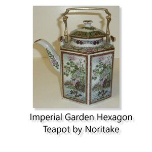 Könnte beinhalten: Eine weiße sechseckige Teekanne mit goldenem Henkel und Deckel. Die Teekanne ist mit einem floralen Muster in Rosa-, Grün- und Blautönen verziert. Die Teekanne ist mit "Imperial Garden Hexagon Teapot by Noritake" beschriftet.