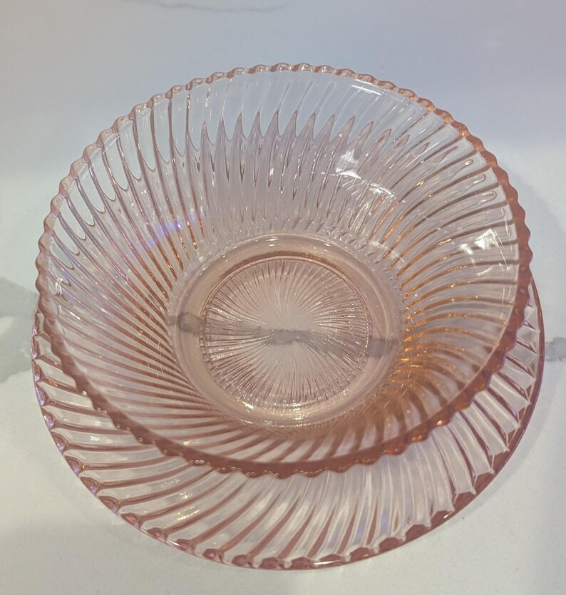 May include: A set of two pink glass bowls. The bowls have a spiral design and a scalloped edge. The bowls are made of a clear pink glass.