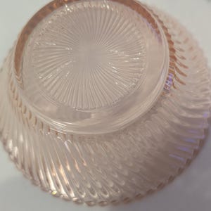 May include: A clear, pink-tinted glass bowl with a spiral design on the exterior and a starburst pattern on the base. The bowl's rim is slightly thicker than the rest of the glass, and the bowl is turned upside down.