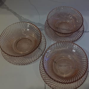 May include: Three pink glass bowls and matching plates. The bowls and plates have a spiral design. The bowls are stacked on top of the plates. The glass is a light pink color.