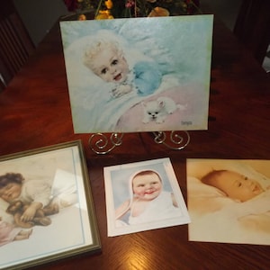 Puede incluir: Tres imágenes enmarcadas de bebés durmiendo. Cada imagen está en un marco simple de madera clara. La imagen superior muestra un bebé con un gatito blanco. La imagen del medio muestra un bebé con un oso de peluche. La imagen inferior muestra un bebé durmiendo en una manta blanca.