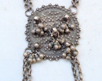 May include: A silver necklace with a large, round pendant featuring a textured design and multiple small beads. The pendant is attached to a chain with multiple strands.
