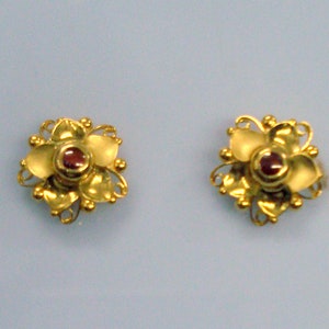 Può includere: Un paio di orecchini d'oro con un design floreale e una pietra preziosa rossa al centro di ogni fiore.