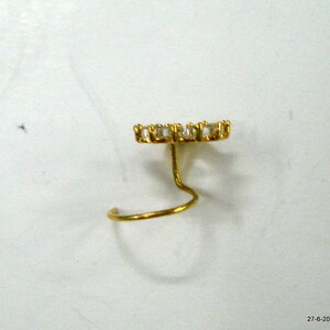 May include: A gold nose ring with a clear crystal design. The ring is a simple, curved shape with a small, round crystal at the top.