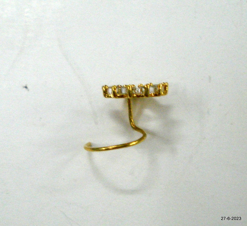 May include: A gold nose ring with a clear crystal design. The ring is a simple, curved shape with a small, round crystal at the top.